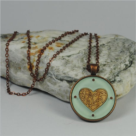 Circle pendant necklace featuring a Kowhaiwhai heart design in green, crafted from etched bamboo and vibrant acrylic.