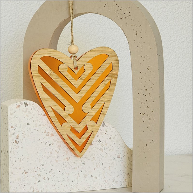 Heart-shaped hanging ornament in orange satin acrylic featuring intricate Koru designs, perfect for home decor or gifts.