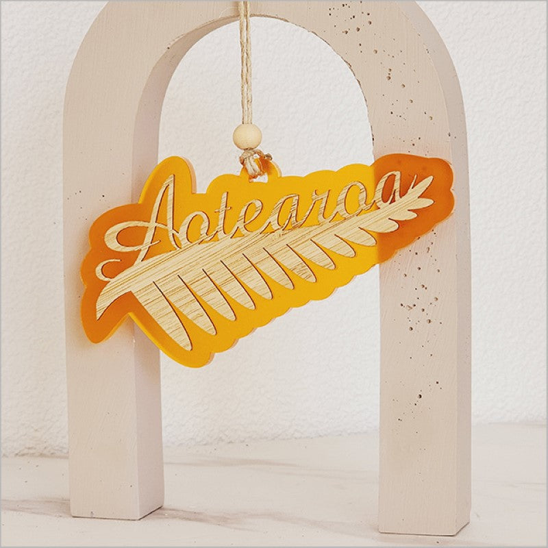 Vibrant orange satin acrylic hanging ornament featuring detailed silver fern design, perfect for holiday decor.