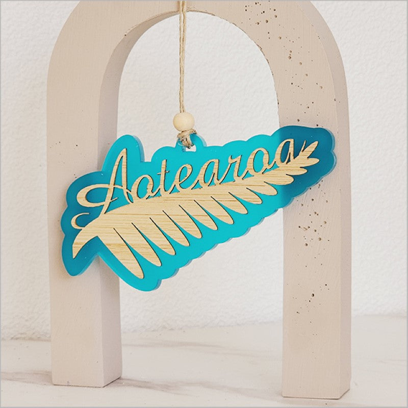 Teal satin acrylic hanging ornament shaped like a silver fern, measuring 130mm x 70mm, perfect for home decor.