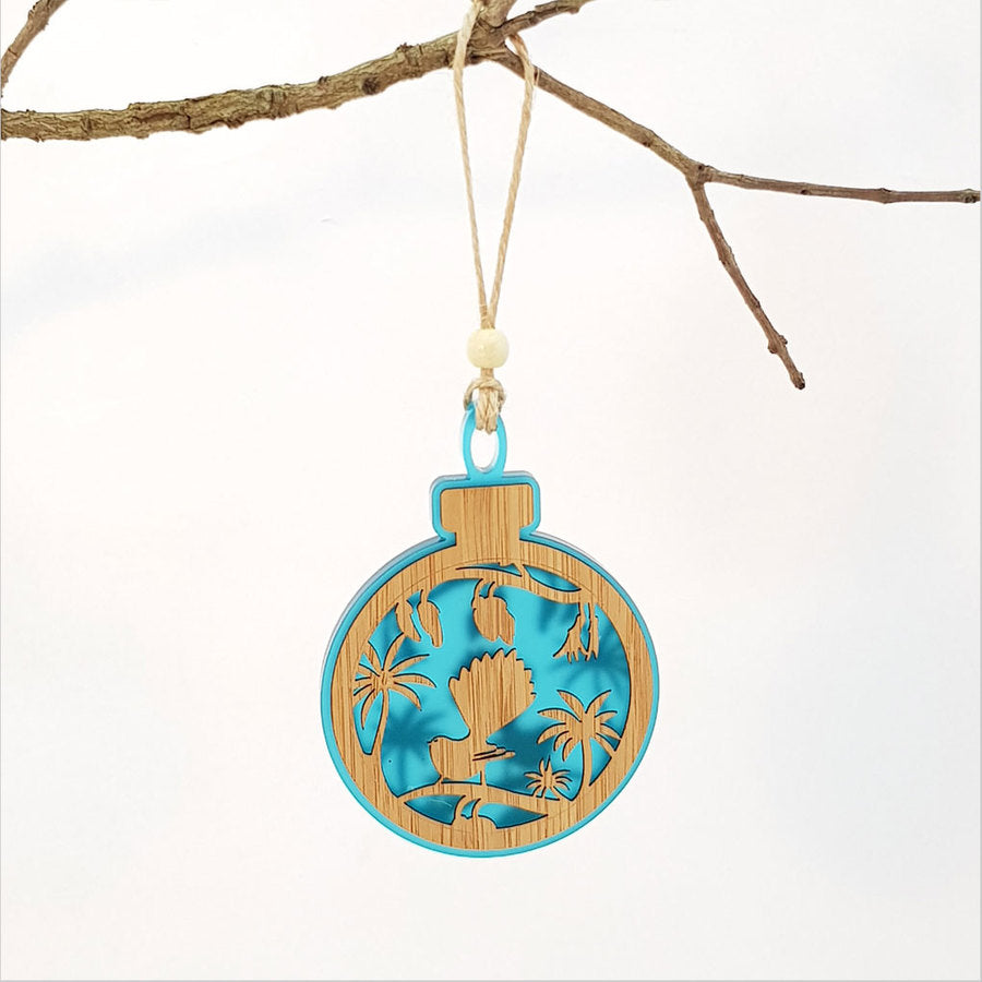 Teal acrylic bauble ornament featuring a fantail on a kowhai branch, perfect for home decor and gifting.