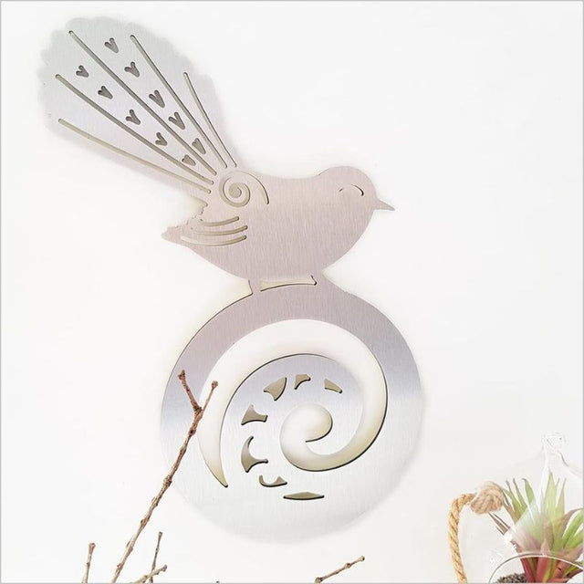 Brushed silver wall art featuring a fantail on koru, 42cm, ideal for indoor/outdoor decor, symbolizing joy and harmony.
