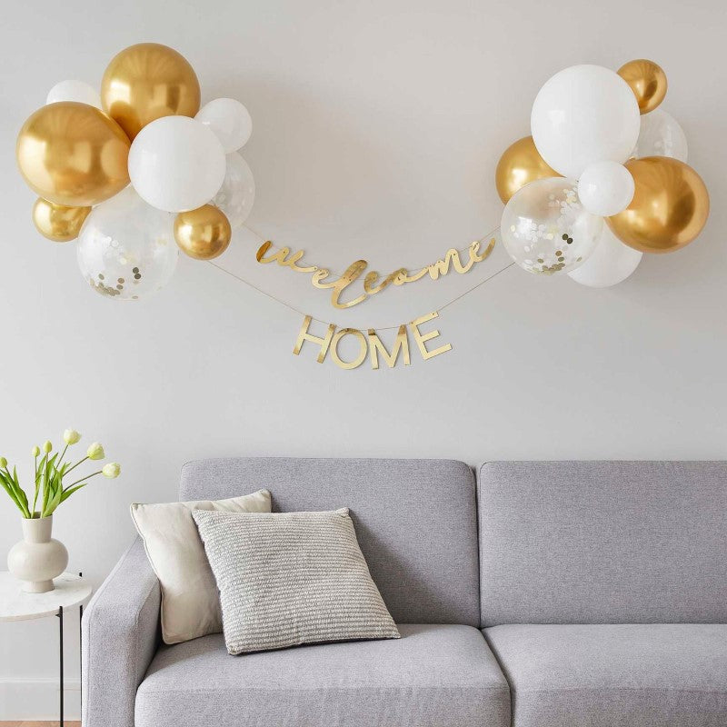 Gold and white balloon backdrop kit with 'Welcome' and 'Home' bunting for a baby’s arrival celebration.
