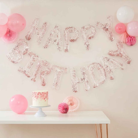 Clear foil letter balloons spelling 'Happy Birthday' with confetti, strung on rose gold twine; perfect for parties.