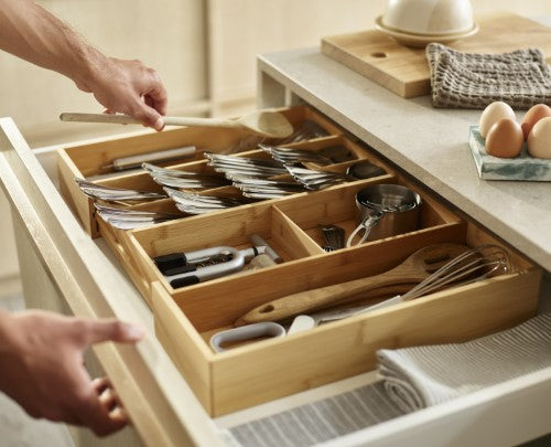 Bamboo drawer organiser with overlapping compartments for cutlery and gadgets, expandable to fit various drawer sizes.