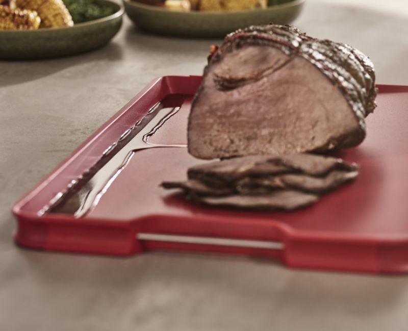 Joseph Joseph Cut & Carve Plus Large Red chopping board with angled base, integrated meat grip, and easy-pour corners.