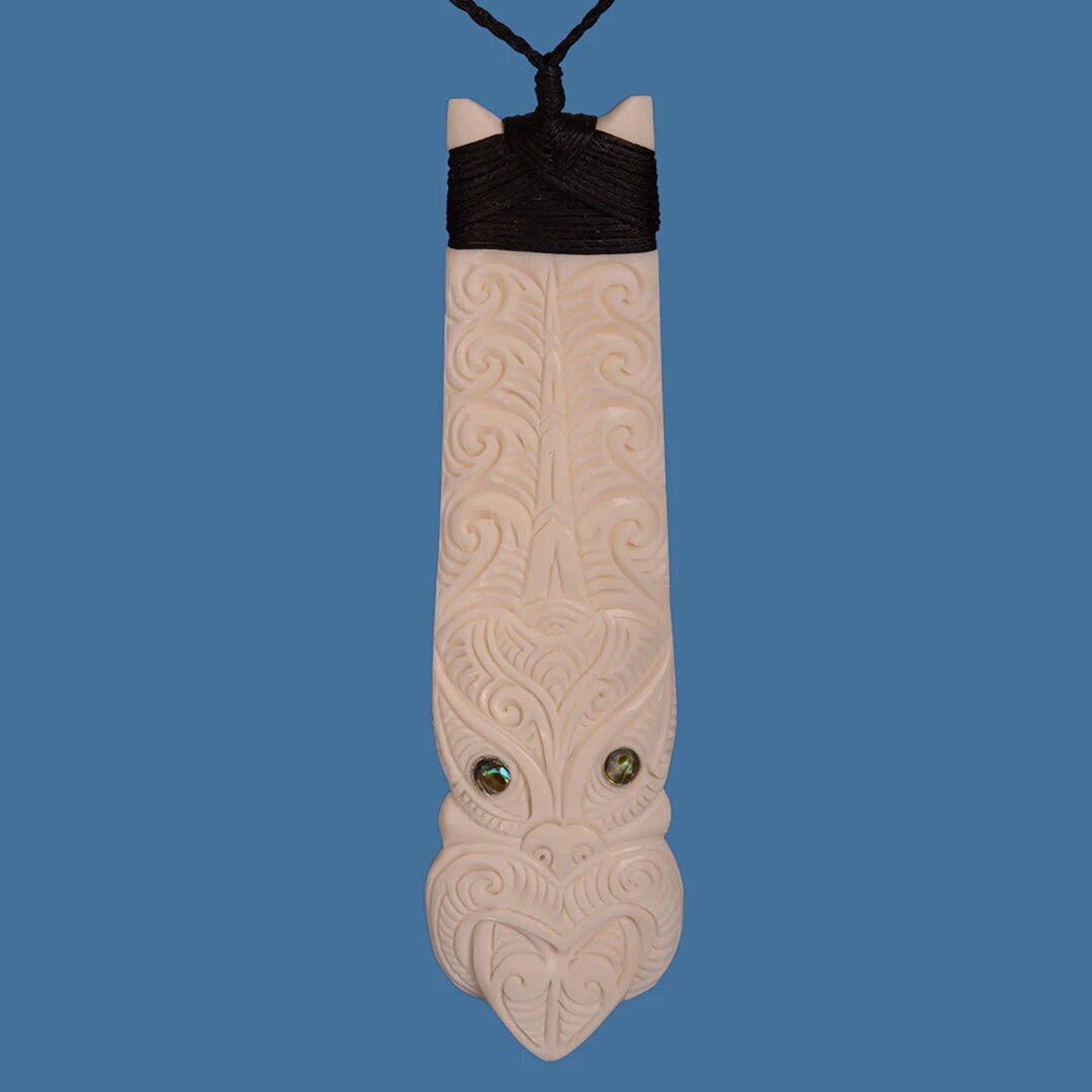 Bone Toki earrings featuring a Tiki face and paua shell accents, celebrating Maori heritage and handcrafted artistry.