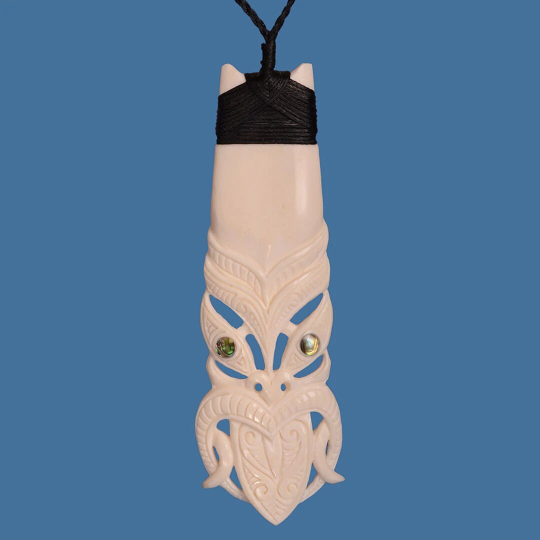 Hand-carved Bone Toki pendant with Tiki pattern, symbolizing Maori craftsmanship and resilience, on adjustable cord.