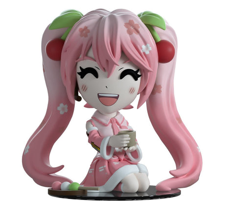 Youtooz Sakura Miku vinyl figurine in pink outfit, kneeling with tea, adorned with sakura blossoms and cherries.