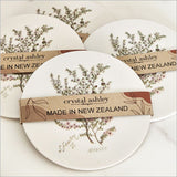 Acrylic coaster featuring a vibrant watercolor illustration of Manuka flowers by Sarah Featon, 10cm diameter with cork base.