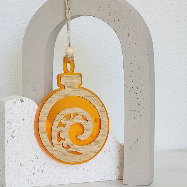 Vibrant orange satin acrylic bauble ornament featuring a koru design, symbolizing growth, perfect for holiday decor.