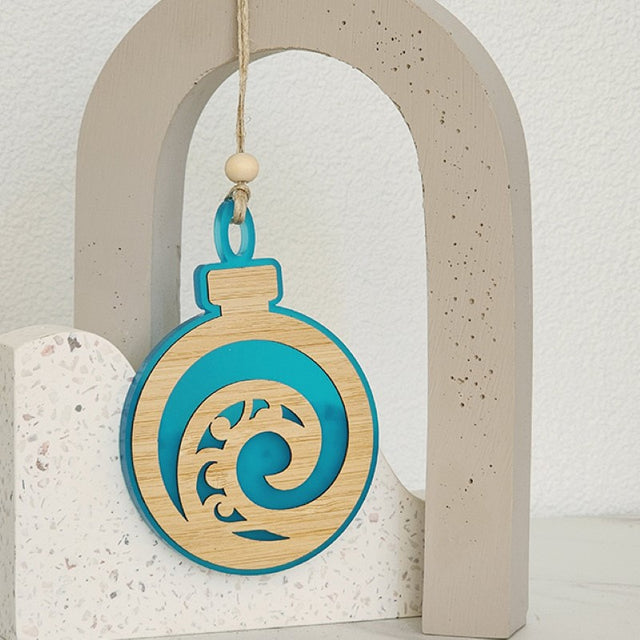 Teal satin acrylic bauble ornament featuring intricate Koru designs, perfect for festive decor or as a thoughtful gift.