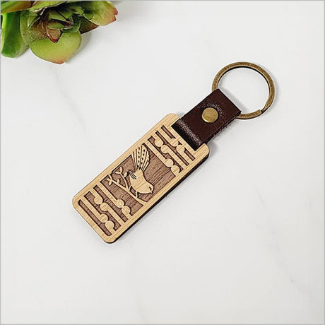 Eco-friendly bamboo keyring featuring intricate Fantail and Koru designs, symbolizing New Zealand's natural beauty.