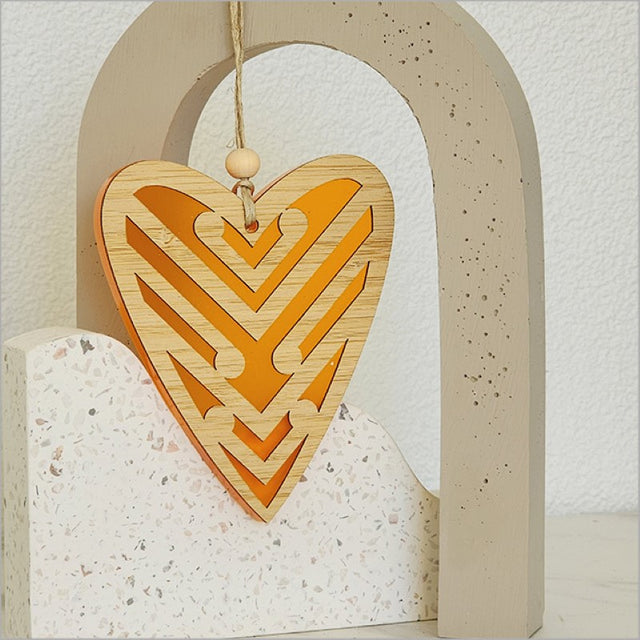 Heart-shaped hanging ornament in orange satin acrylic featuring intricate Koru designs, perfect for home decor or gifts.