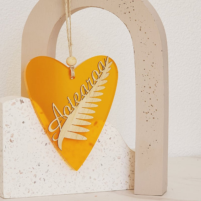 Vibrant orange satin acrylic heart ornament featuring intricate silver fern designs, perfect for home decor or gifting.
