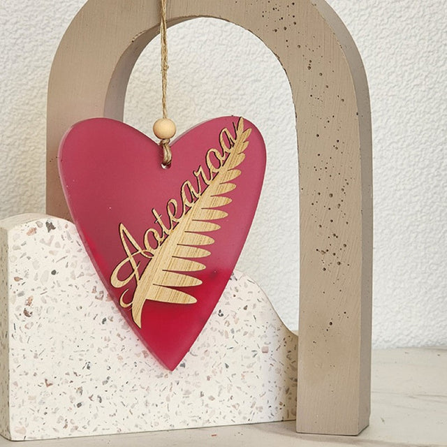 Heart-shaped hanging ornament in pink satin acrylic with silver fern design, perfect for elegant home decor.