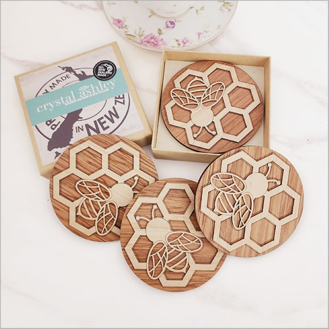 Handcrafted bamboo and rimu coasters featuring intricate bee designs, perfect for protecting surfaces from moisture.