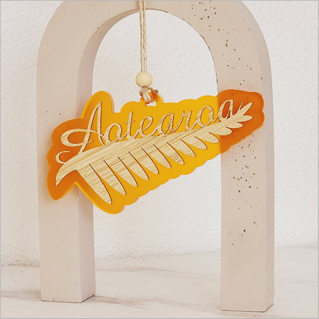 Vibrant orange satin acrylic hanging ornament featuring detailed silver fern design, perfect for holiday decor.