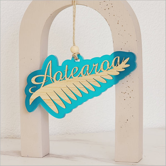 Teal satin acrylic hanging ornament shaped like a silver fern, measuring 130mm x 70mm, perfect for home decor.