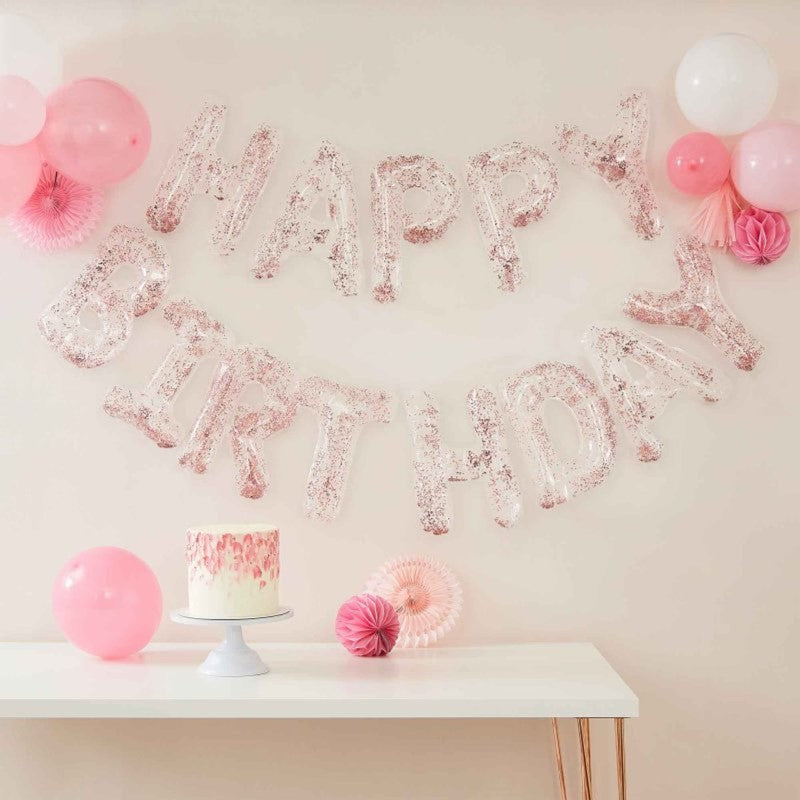 Clear foil letter balloons spelling 'Happy Birthday' with confetti, strung on rose gold twine; perfect for parties.