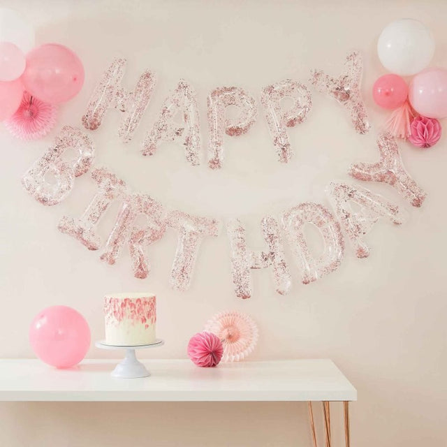 Clear foil letter balloons spelling 'Happy Birthday' with confetti, strung on rose gold twine; perfect for parties.
